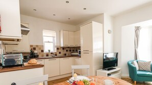 A modern kitchen with a toaster, a bowl of fruit, and a dining table set for breakfast. - Marina Reach (Weymouth)