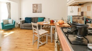 A modern kitchen with a dining area, a sofa, and a teal armchair. - Marina Reach (Weymouth)