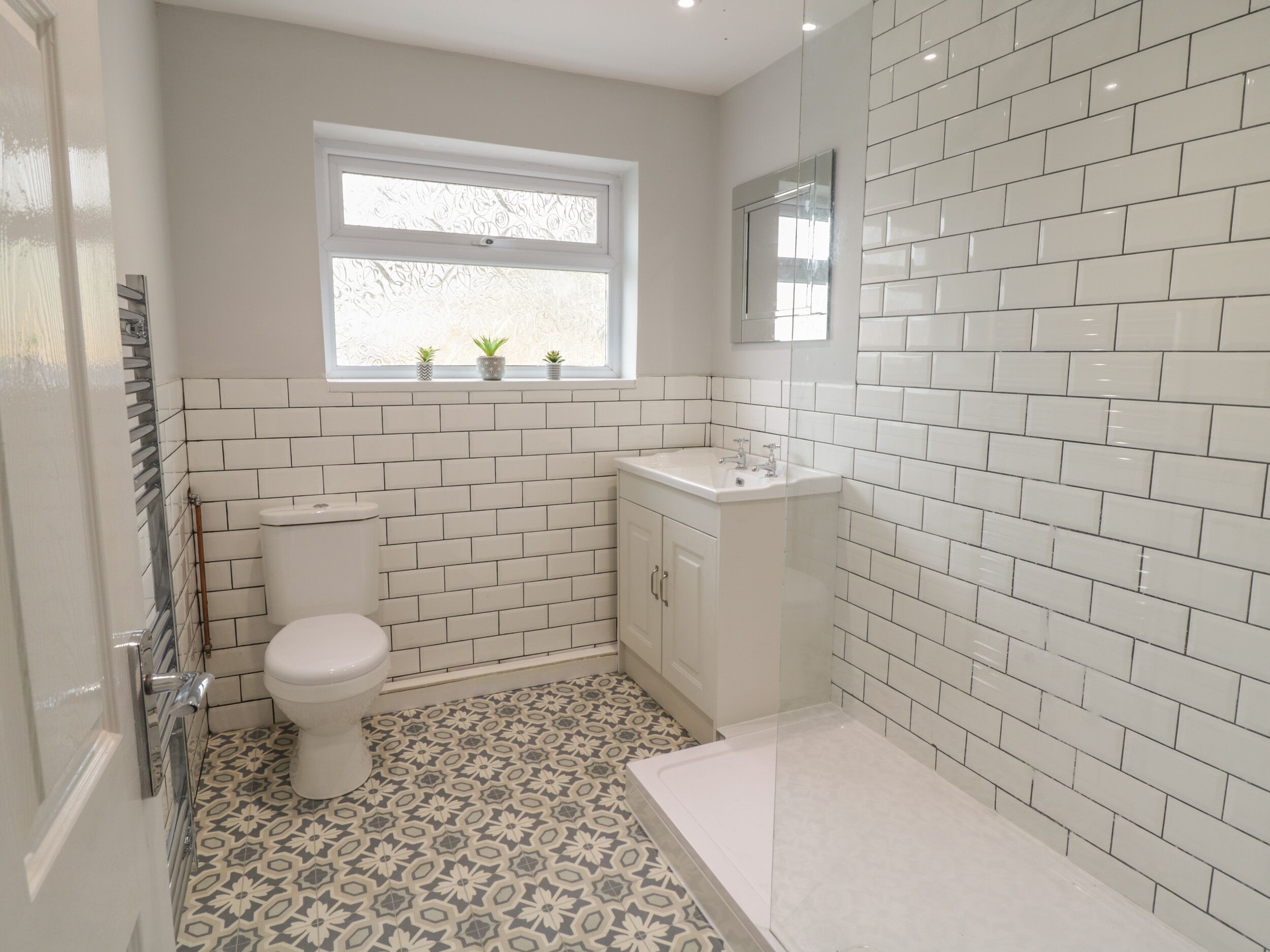 A bathroom with white tiled walls, a toilet, a sink, and a shower area.
