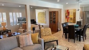 A spacious living room with a sofa, armchairs, a dining table, and a kitchen area with a refrigerator and cabinets.