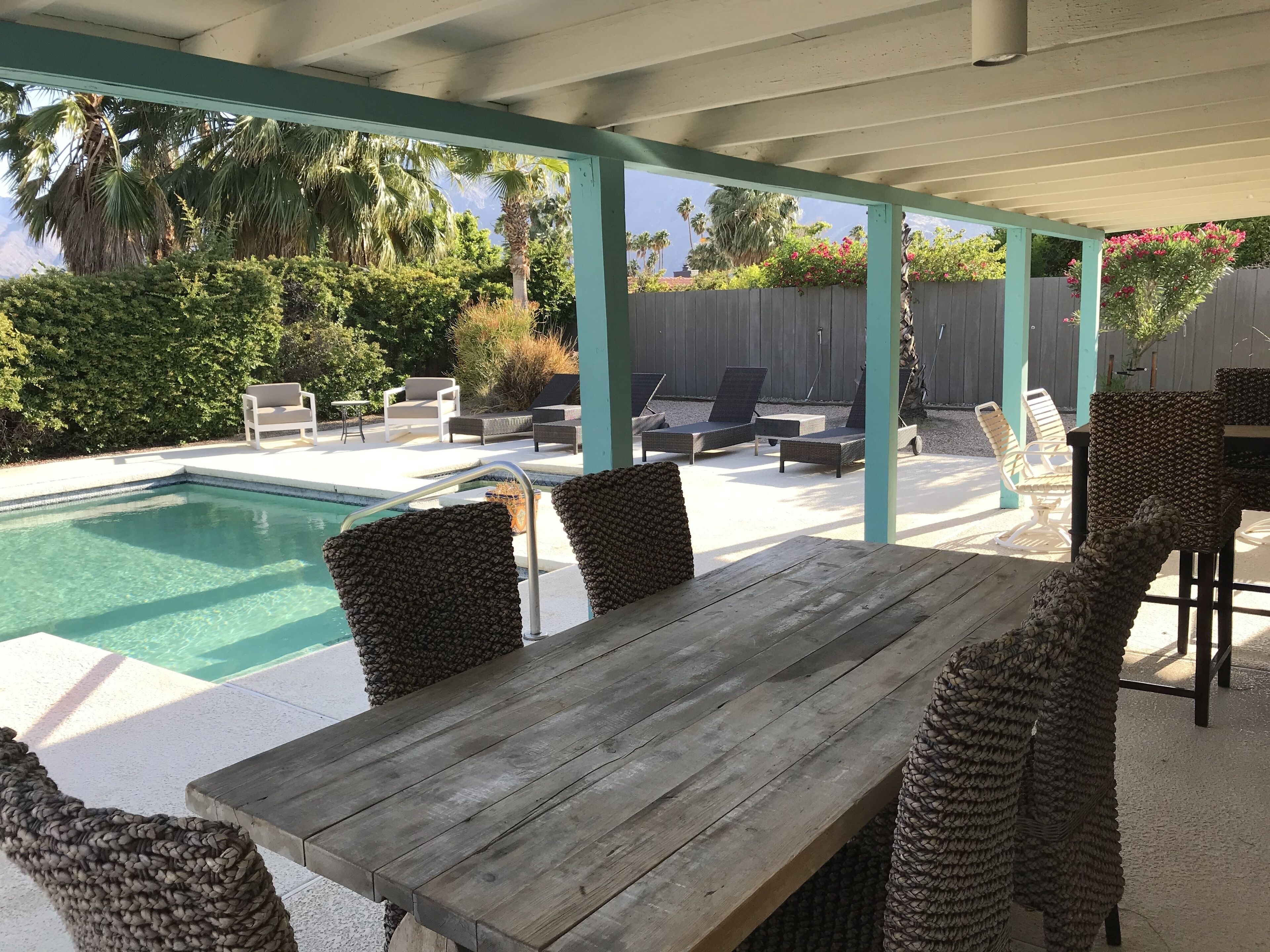 A covered outdoor area with a pool, lounge chairs, and a wooden table.