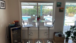 Una cocina con una mesa de vidrio y dos taburetes de bar, un microondas y una cesta de toallas.