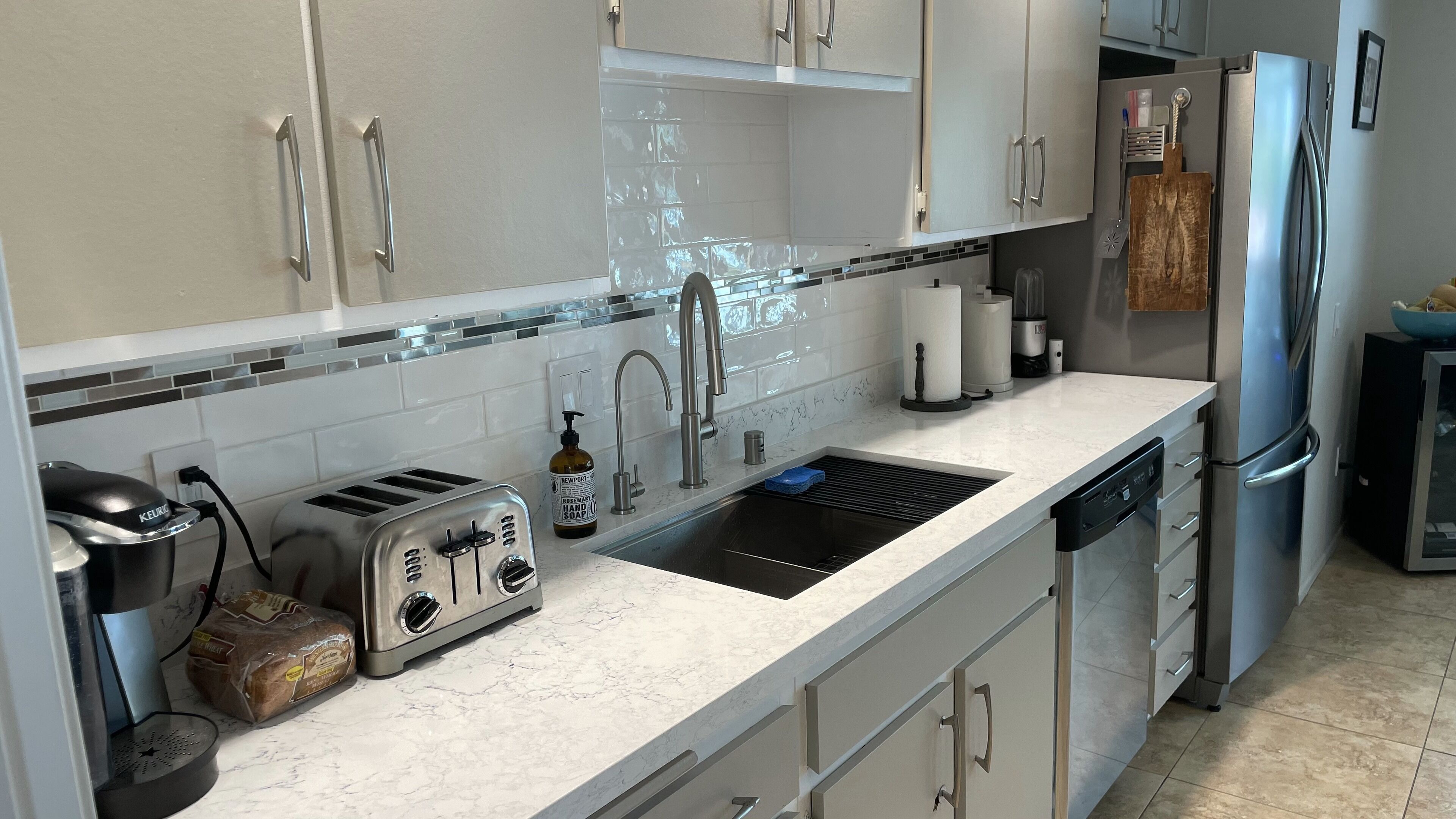 A modern kitchen with white cabinets, a stainless steel sink, a toaster, and a dishwasher.