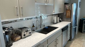 Una cocina moderna con armarios blancos, un lavamanos de acero inoxidable, un tostador y un lavavajillas.