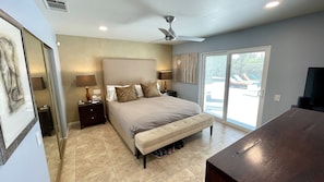 A bedroom with a bed, two bedside tables, a ceiling fan, a large window, and a view of a pool.