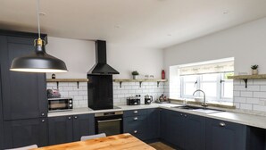 A modern kitchen with dark cabinets, a wooden table, and a black range hood. - Holida Hoose (Belford)