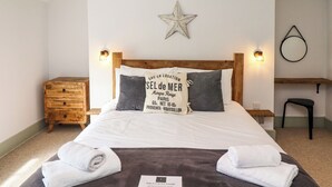 A neatly made bed with white linens and two folded towels, a wooden nightstand with a lamp, a small wooden dresser, and a wall-mounted star decoration. - Holida Hoose (Belford)