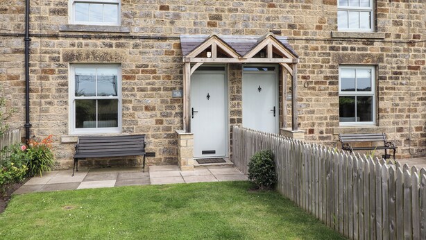 A stone building with two doors, a bench, and a wooden fence. - Holida Hoose (Belford)