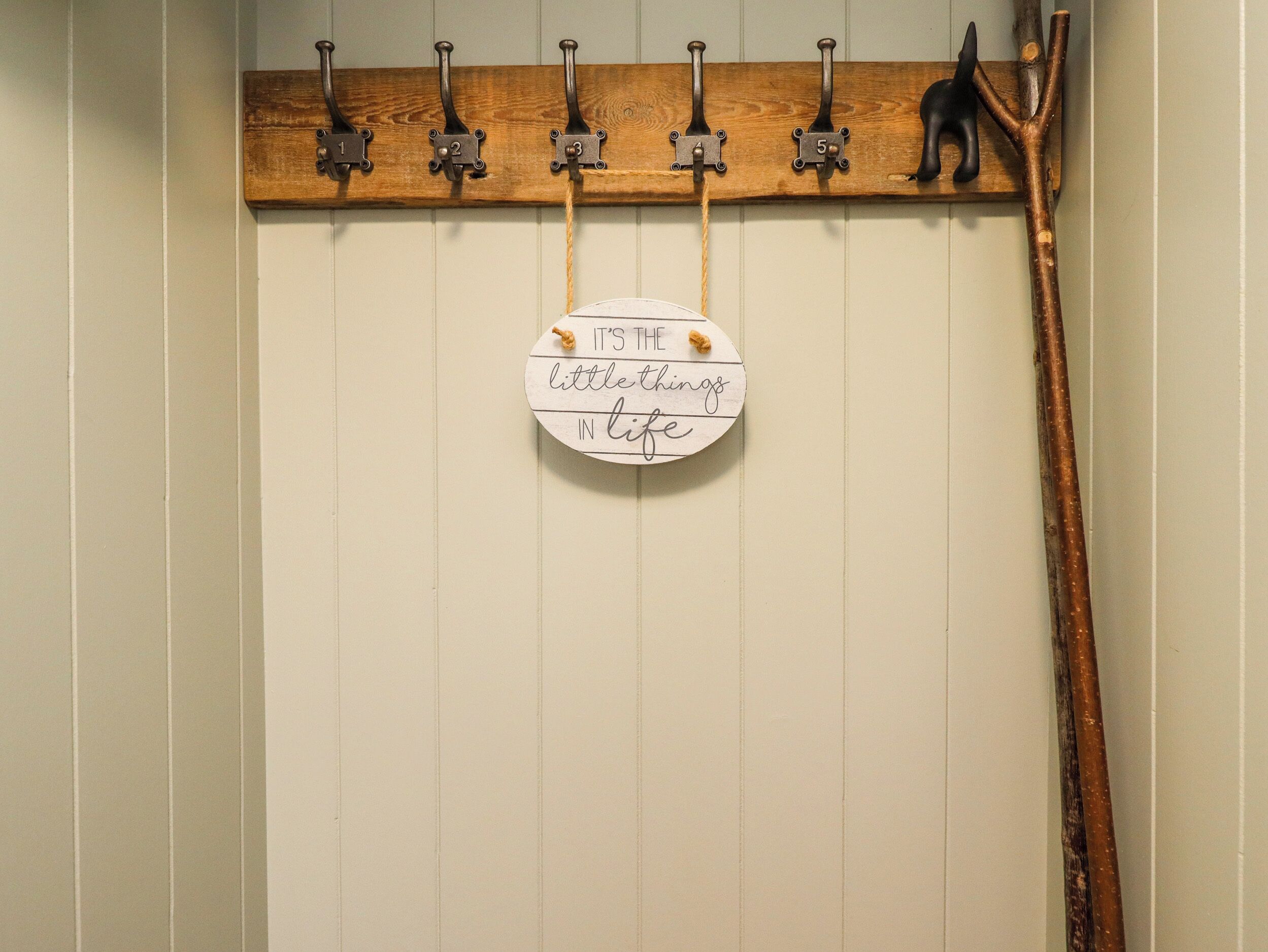 Eine Wand mit einem hölzernen Kleiderhaken, der sechs Haken und ein Schild mit der Aufschrift "It's the little things in life" zeigt.