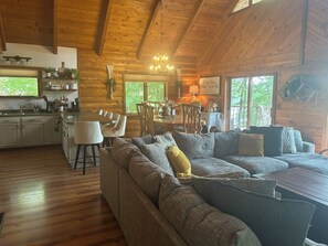 A cozy cabin interior with a wooden ceiling, a dining area with chairs and a table, a sofa with cushions, and a kitchen with a sink and cabinets. - The Little Rascals Lake House (Cameron)