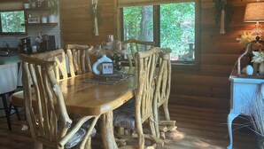 A rustic wooden dining area with a chandelier, wooden chairs, and a table with a placemat. - The Little Rascals Lake House (Cameron)