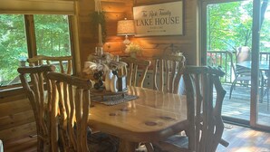 A wooden dining area with a chandelier, rustic chairs, and a table set for six. A sign reads "The Rook Family Lake House." - The Little Rascals Lake House (Cameron)