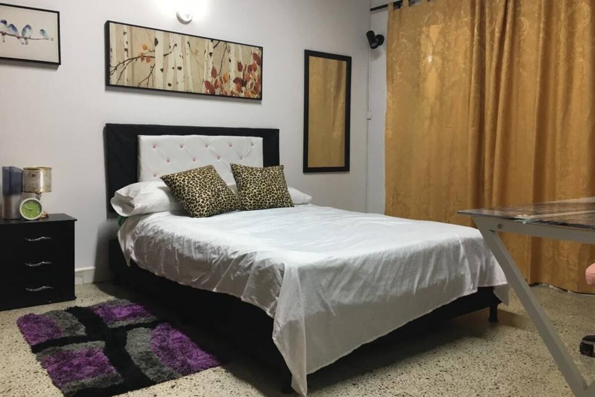 A bedroom with a bed, a nightstand, a lamp, and a wall with artwork.