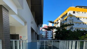 A swimming pool with a glass barrier and metal handrails, surrounded by a modern building with balconies and a clear blue sky. - Beautiful apartment in Bacutia (Guarapari)
