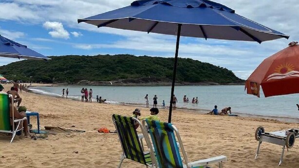 A beach with several beach chairs and umbrellas, a sandy shore, and a body of water in the background. - Beautiful apartment in Bacutia (Guarapari)
