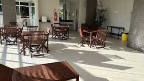 A spacious indoor area with multiple wooden tables and chairs, a bench, and a trash bin. - Beautiful apartment in Bacutia (Guarapari)