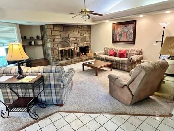 Relax by the fireplace in this inviting living room, featuring a sofa, coffee table, and ceiling fan.