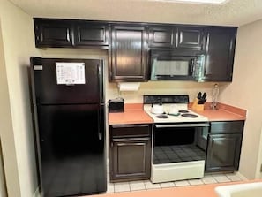 Kitchen area with a stove, refrigerator, microwave, sink, and countertop.