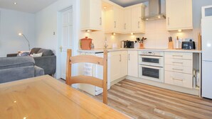 Een kleine keuken met witte kastjes, een houten eettafel en een inbouwoven.