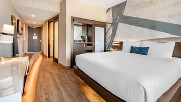 A modern hotel room with a large bed, a seating area, and a kitchenette.