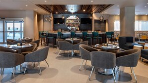 Un restaurante moderno con mesas y sillas redondas, una zona de bar y vistas a la calle.