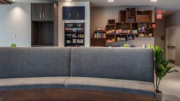 A modern lobby with a grey sofa, a dark wooden cabinet, a shelf with snacks, and a potted plant.