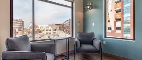 Ein modernes Zimmer mit zwei grauen Sesseln, einem kleinen Tisch und großen Fenstern mit Blick auf die Stadt.