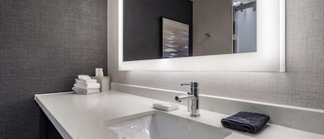 A modern bathroom with a white sink, a large mirror, and a towel rack.