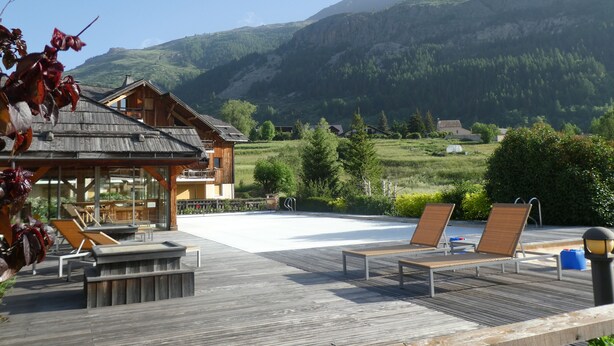 Un edificio de madera con balcón, una terraza de madera con sillones de descanso y vistas a un paisaje montañoso.