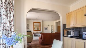 A modern kitchen with wooden cabinets, a microwave, and a dining area with a glass table and chairs. - Harbour View (Pwllheli)