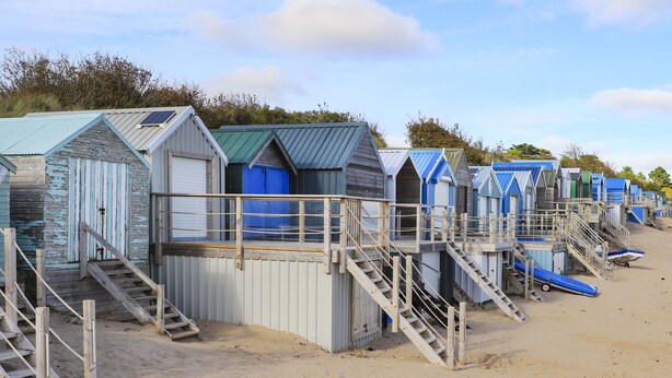 A row of beach huts with wooden stairs leading to the entrance, situated on a sandy beach. - Harbour View (Pwllheli)