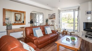 A spacious living room with a brown leather sofa, a glass coffee table, and a television. - Harbour View (Pwllheli)