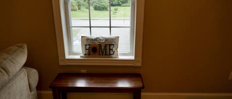 A room with a window, a bench, and a cushion with 'welcome to our HOME' text.