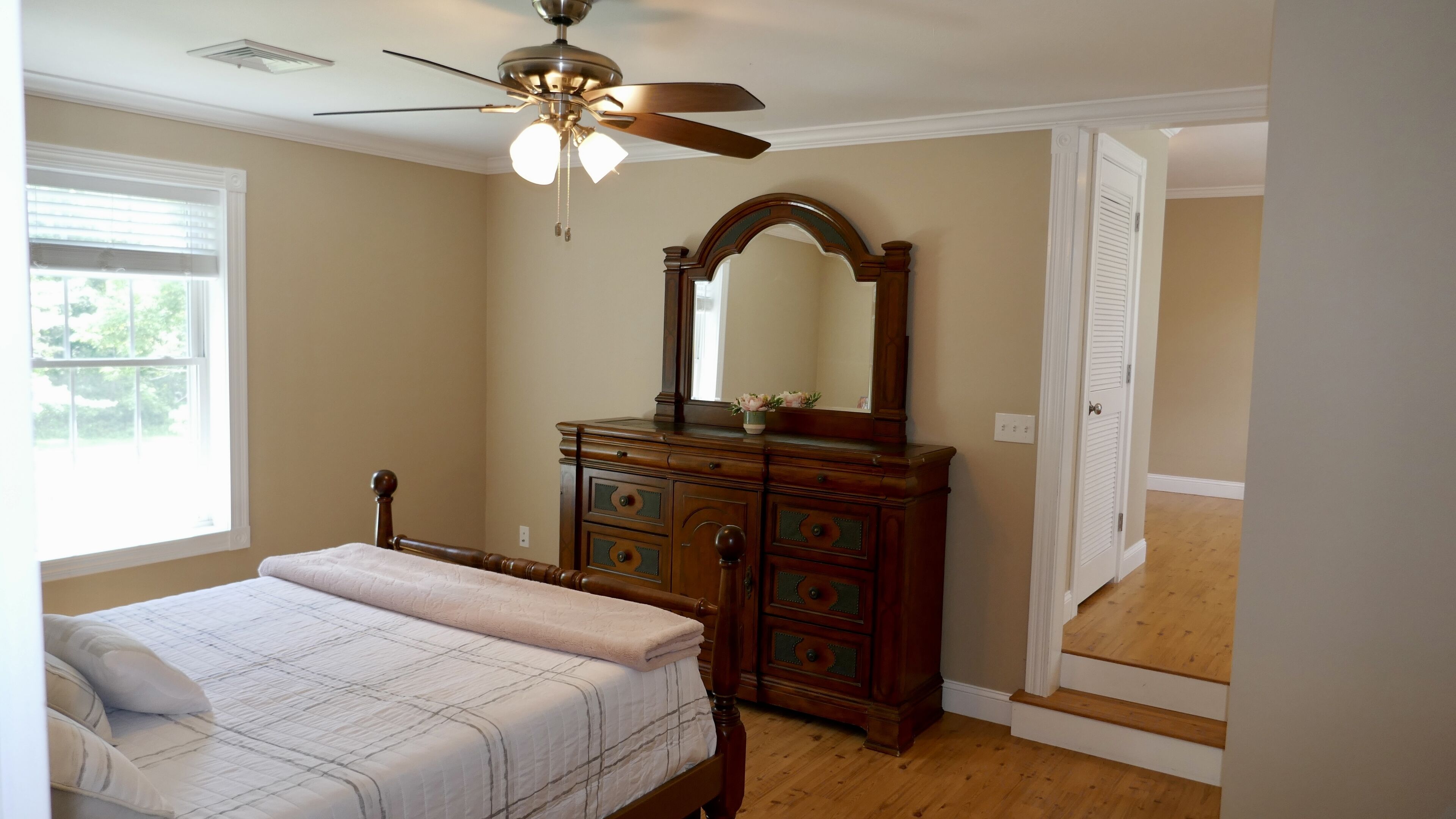 A bedroom with a bed, a dresser, a ceiling fan, and a door leading to another room.