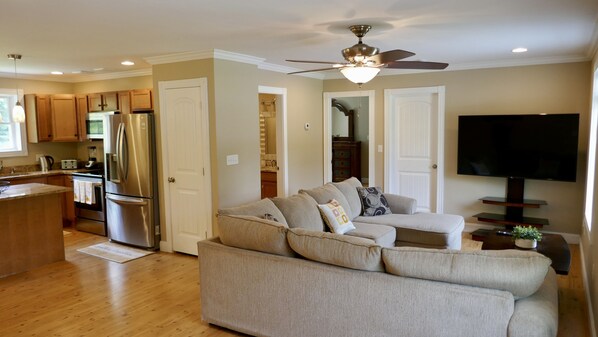 A modern kitchen with stainless steel appliances, a wooden dining area, and a living room with a large TV and a ceiling fan. - Travel light long-term (safe & relaxing )special discount for travel nurse (Veazie)