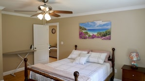 A bedroom with a bed, a ceiling fan, a nightstand, a lamp, and a painting on the wall.