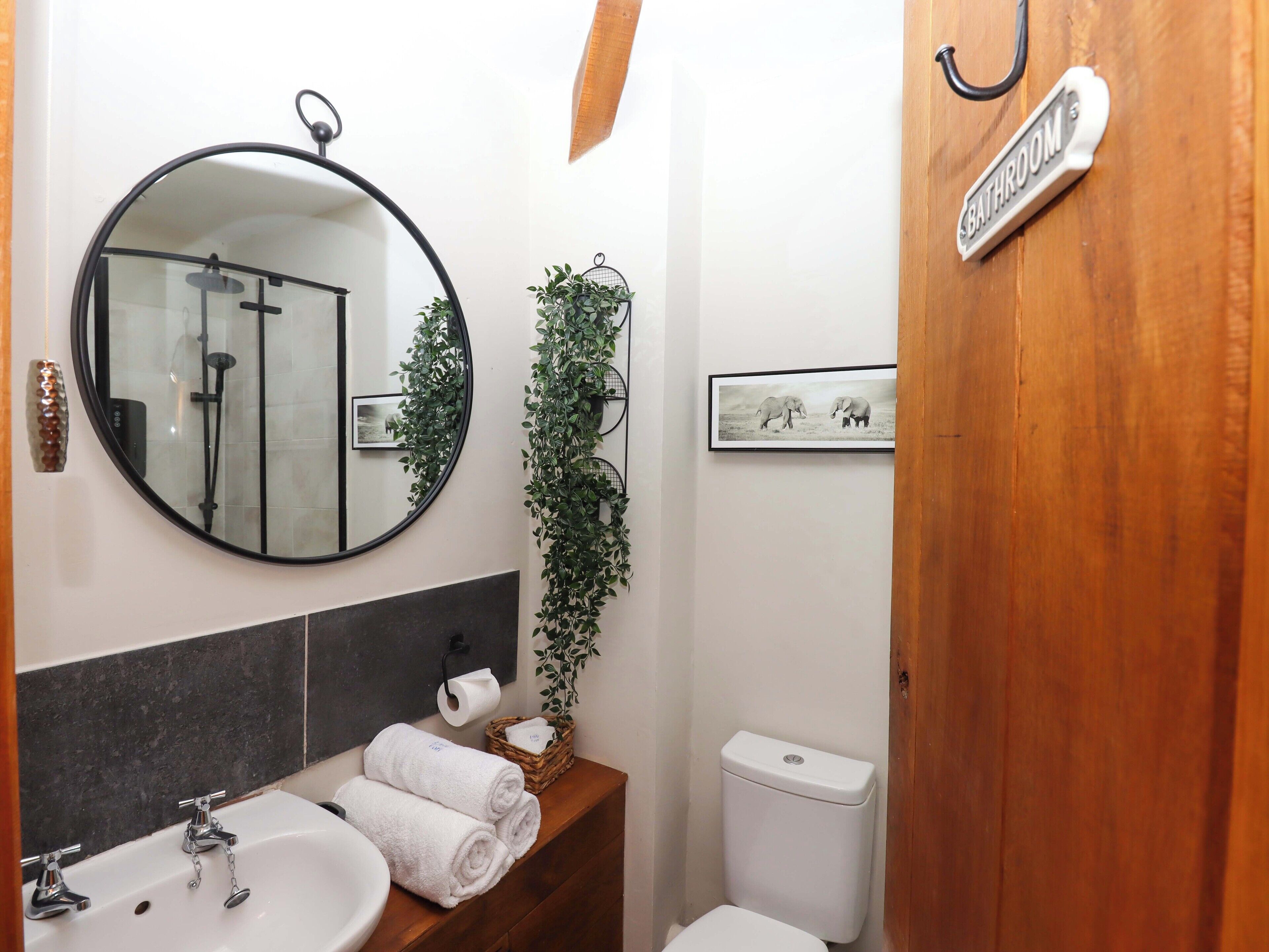 A bathroom with a round mirror, a sink, a toilet, and a wooden door labeled "BATHROOM".