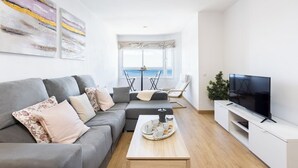 A modern living room with a grey sofa, a coffee table with a tray, a flat-screen TV, and a view of the sea through a window. - Home2Book Comfy Beachfront Radazul (Radazul)