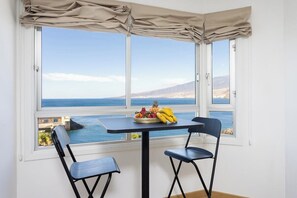 Zona pranzo con tavolo e due sedie, una finestra vista mare e un cesto di frutta sul tavolo.
