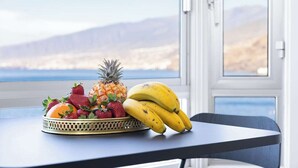 A table with a fruit basket containing strawberries, pineapple, and bananas, and a chair with a view of a mountainous landscape through a window. - Home2Book Comfy Beachfront Radazul (Radazul)