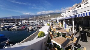 A marina with boats docked, outdoor seating, and a view of the city and mountains in the background. - Home2Book Comfy Beachfront Radazul (Radazul)