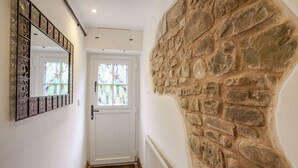 Un pasillo con una puerta blanca, un muro de piedra y un espejo decorativo.