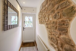 Un pasillo con una puerta blanca, un muro de piedra y un espejo decorativo.