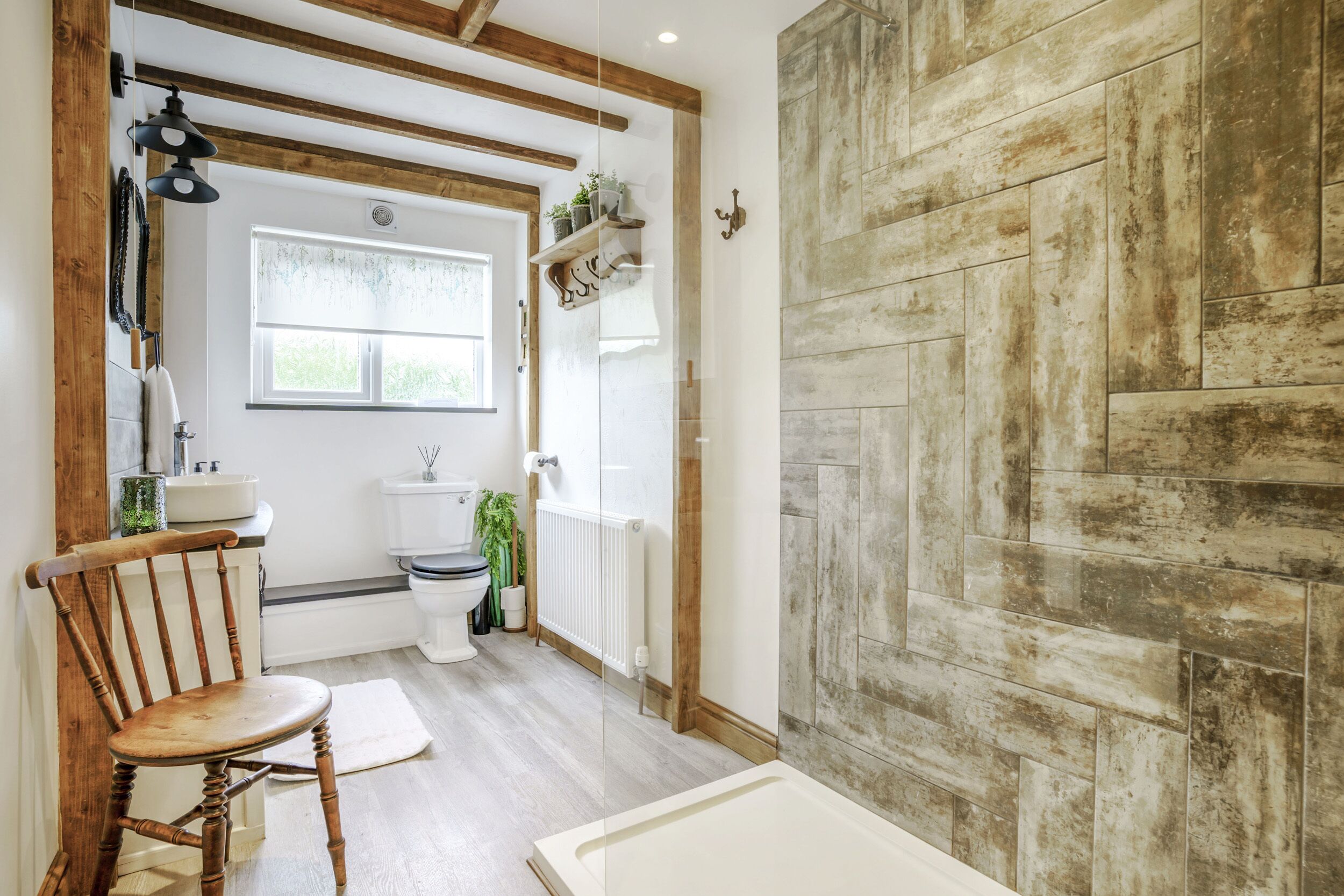 A bathroom with a wooden chair, a white bathtub, and a rustic wall.