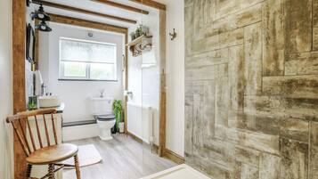 A bathroom with a wooden chair, a white bathtub, and a rustic wall.