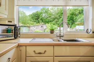Una cocina con un ventanal grande, un lavamanos y un microondas.