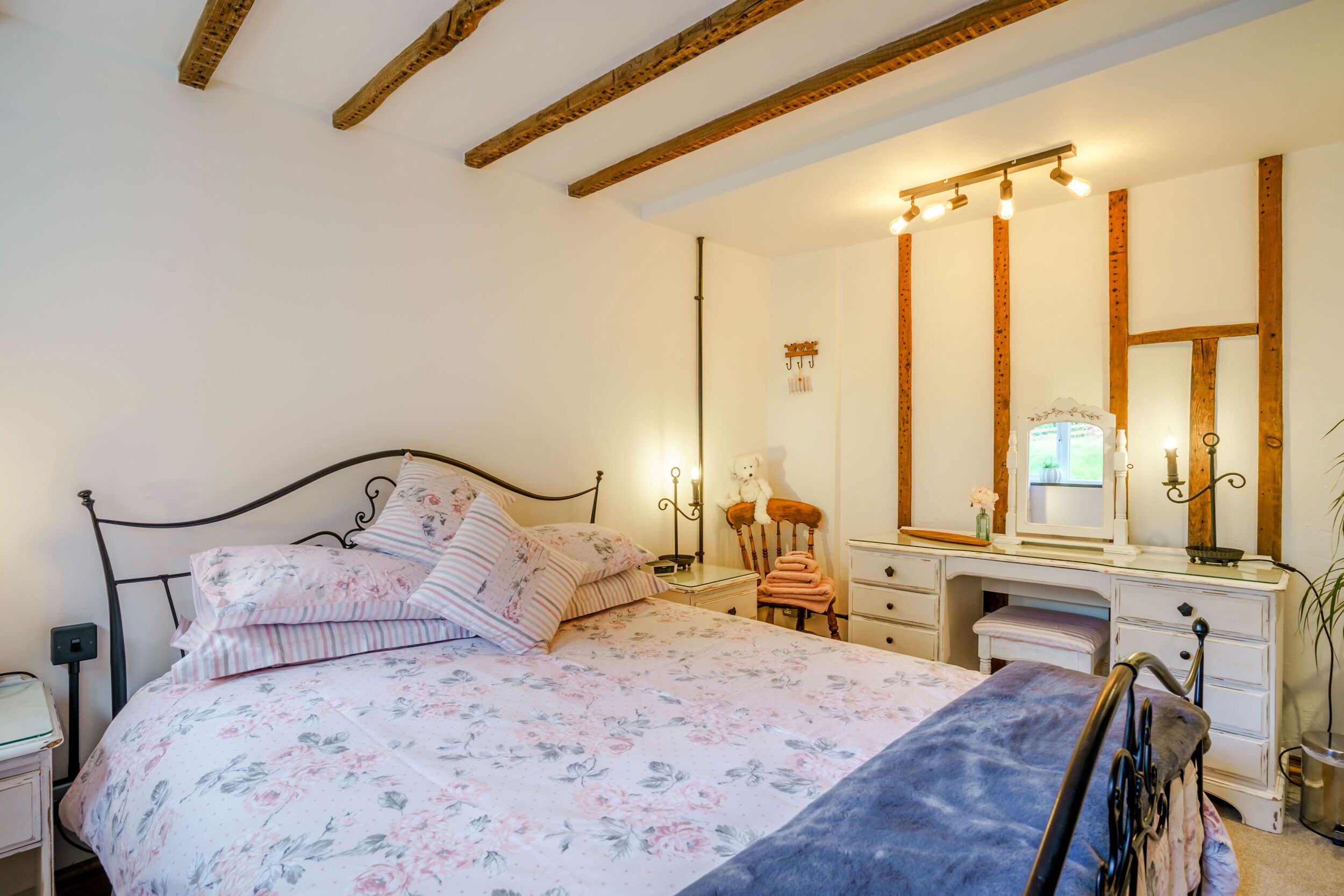 A bedroom with a bed, a dresser, a vanity with a mirror, and a chair.