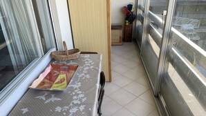 Un piccolo balcone con un tavolo ricoperto da una tovaglia floreale, un cesto in vimini e un vassoio di frutta.