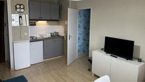 Un ambiente compatto con angolo cottura, zona pranzo e televisione su un mobiletto.