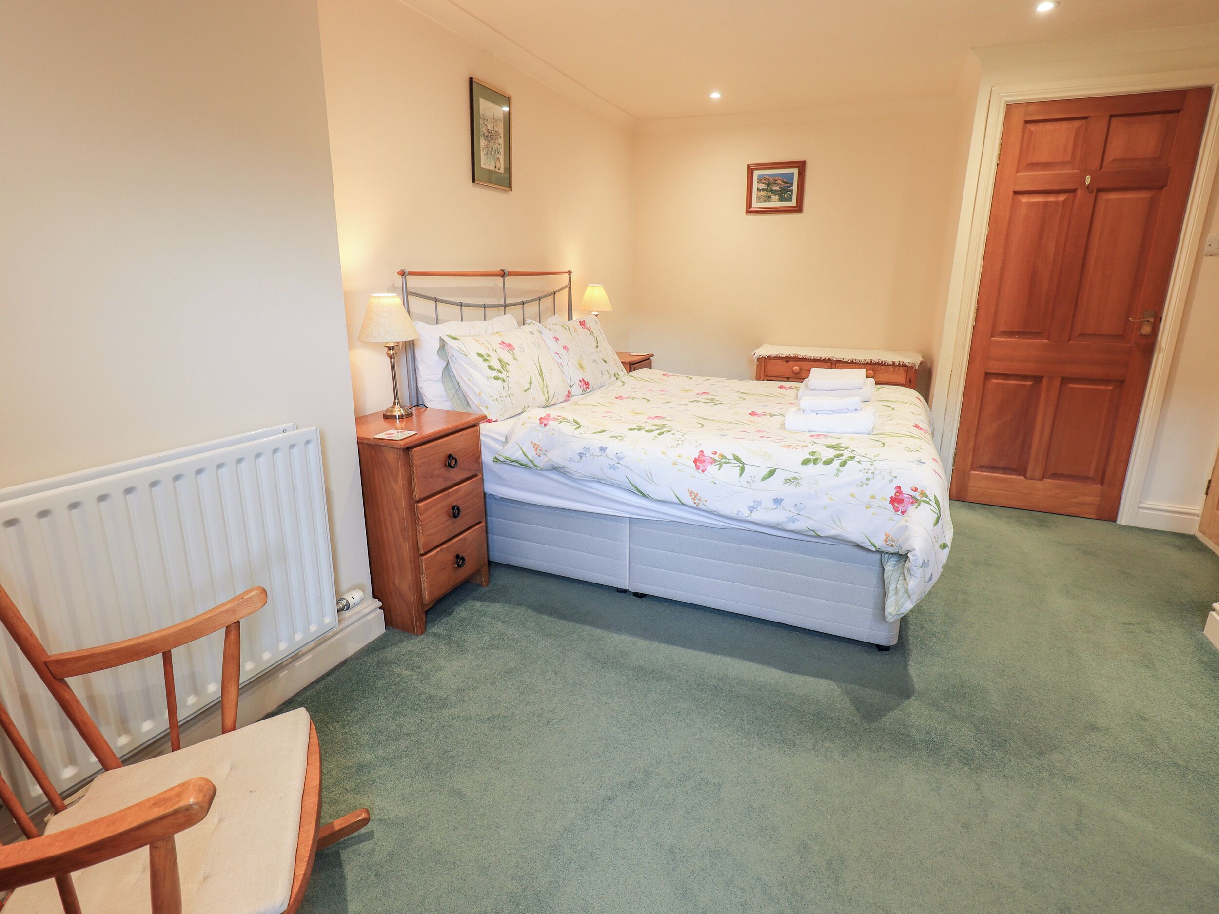 A bedroom with a bed, a wooden nightstand, a chair, and a radiator.